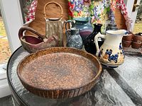 Photo showing multiple ceramic pottery items arranged on a table including vases, pitcher, shallow bowl, and decorative bird-shaped item.