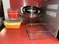 Various Pyrex covered dishes in orange and yellow, clear glass mixing bowls stacked inside each other, stainless steel mixing bowls on top