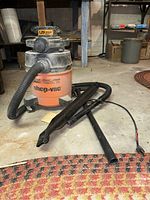 Full view of the orange and black Shop Vac unit with attached hose and several black attachments on floor.