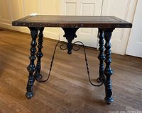 Side angle view of the wooden side table showing wood top, metal edging with rivets, turned legs, and decorative metal stretcher.