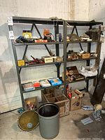 Wide shot of metal shelving unit containing various hardware boxes, tools, and storage crates on floor nearby.