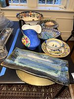 View of entire collection showing large blue-glazed rectangular tray, floral pitcher, Quimper bowl and various plates and bowls with colorful patterns.