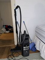 Full view of Lux vacuum cleaner with hose, wand, floor nozzle attached, broom and dustpan beside bed
