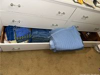 Open dresser drawers showing stacks of blue knit blanket and folded towels inside drawers.