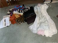 Overview of various scarves, handbags, slips, and stockings arranged on carpeted floor.