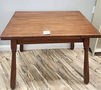 Front-facing photo of rectangular wooden antique table with four turned legs against a plain background on wood patterned floor.