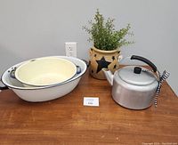 Photo showing antique ceramic basin and dish pan with blue rim accents, aluminum tea pot, and beige star crock with faux greens on wooden surface