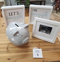 Lot displayed on wooden table with all items visible: piggy bank, two snuggle signs, and framed ultrasound photo frame