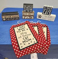 Photo of 3 new wooden cat signs with humorous cat sayings and 3 matching red floral and cream tea towels with cat mom text and paw prints.