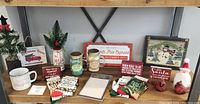 Full display of assorted new Christmas decoration items including mugs, candles, decorative signs, socks, and figurines arranged on shelf.