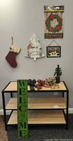 Wide view of the Christmas decor items displayed on a wooden shelf including a green welcome sign, small tree, bows, floral wreath, stocking, and decorative wooden tree