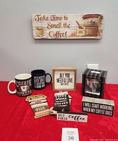 Photo showing coffee signs, mugs, fabric coozies, socks and teapot nightlight arranged on table with red cloth.