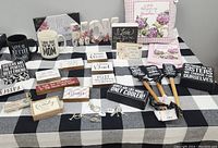 Table with an assortment of new family-themed gift items including mugs, signs, plaques, pillows, and garden tools arranged neatly.