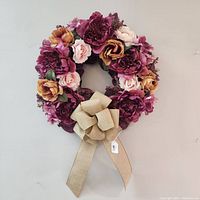 Front view of handmade floral wreath with purple, pink, and peach flowers, and a burlap bow at the bottom.