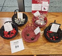 Photo showing five small woven baskets each containing different Ganz charms: lighthouse, cardinal, ladybug, turtle, and Christmas cardinal, with informational tags in each basket.