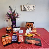 Photo of Halloween decorating lot on red tablecloth showing multiple items including signs, socks, metal jack-o-lantern, floral boot arrangement, and small decorations