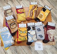 Photo shows 12 pairs of Primitives by Kathy socks arranged with each mismatched pair displaying food-themed patterns including bacon, eggs, peanuts, nachos with mustard, salt and pepper, coffee and donuts, and strips of bacon.