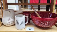 Photo showing all items in the Rae Dunn Christmas set: Hot Cocoa pitcher, FA LA LA mug, NORTH POLE mug, SANTA'S COOKIES bowl, and Ho Ho Ho spatula.