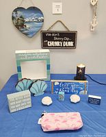 Close-up photo of tabletop seashore themed pieces including wooden signs, shell-shaped dishes, night light or candle holder, blue photo frame, and pink flamingo pouch
