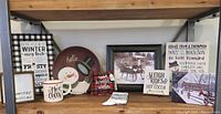 Photo showing various snow themed decor items including signs, mug, socks, small plate, framed winter photo print.