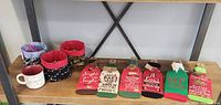 Photo showing three small handmade cloth bins, a white ceramic mug, and six Christmas-themed fabric wine bottle covers on a wooden shelf.