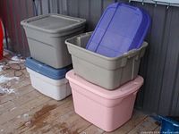 Four Plastic Storage Bins stacked with lids on a wooden surface outdoors near a metal wall.