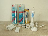 Braun electric toothbrush handle with charger, power cords, universal travel kit adapters, and three packages of replacement brush heads on a wooden surface.