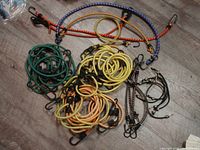 Multiple bungee cords of various colors and sizes coiled on floor showing hooks at ends.