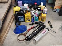 Full overview of all vehicle care items on wooden surface, showing motor oil bottles, spray cans, grease gun, and funnel.