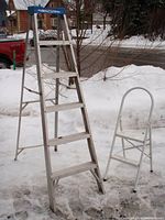 6-foot aluminum step ladder with blue top cap and six steps seen fully opened outdoors with snow in background