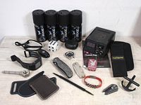 Photo showing 4 cans of Axe body spray, Nike GPS watch, tattoo pen machine, folding knives, multitool, wallet, dice, and other small accessories all arranged on a white surface.