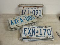 Multiple old Ontario license plates stacked and fanned out on table, showing various plate numbers including JZJ 091, AXFA 085, EXN 170.