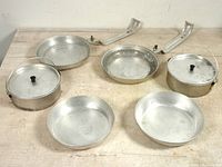 Full view of both sets showing frying pans with removable handles, deep dish plates, and stock pots with lids arranged on table.