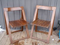 Two vintage wooden folding chairs placed side by side showing front and side view. Both chairs show wear consistent with age.