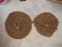 Two coiled metal tow chains with hooks lying flat on concrete. Chains are rusted but intact.