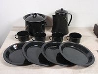 12 piece vintage black enamel camping cook set including stock pot with lid, coffee pot with lid, four coffee mugs and four dinner plates laid out on table.