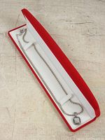 Silver necklace with jewelled square pendant inside red and white gift box, showing overall lot presentation and packaging.