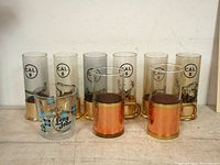Front view of the complete lot showing the seven hunting themed highball glasses, two copper mugs, and one Ballantine's Whiskey glass