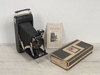 Kodak Junior Six 16 folding camera extended, with original box and instruction manual behind it on a wooden surface