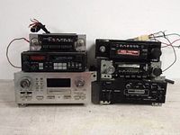 View of six vintage car audio units stacked together showing front panels with cassette slots, tuning knobs, and preset buttons.