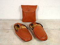 Front view of brown leather moccasin slippers paired with matching leather travel pouch behind them