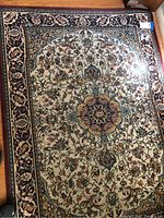 Full top-down view of area rug showing central medallion and intricate floral border on cream background.