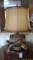 Front view of whiskey barrel lamp showing lamp shade, barrel, musket, lantern, and rope details.