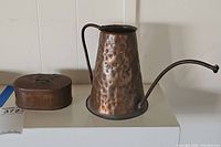 Image showing both the hammered copper watering can with long spout and the small hinged lidded copper box together on a white surface.