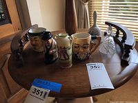 Photo showing a small round wooden table with ceramic character cups, two metal bells, and a glass bell arranged on it.