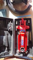 Top-down view of red MVP hydraulic floor jack in black plastic case with accessories in allocated slots.