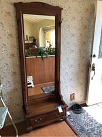 Front view of a wooden hall tree with a large framed mirror, bench with a storage drawer underneath, and side hooks.
