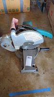 Front-side view of the Makita mitre saw showing saw blade guard, handle, and dust bag.