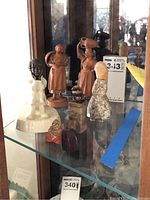 Miniature figurines displayed on glass shelf including carved wood, porcelain and stone figurines