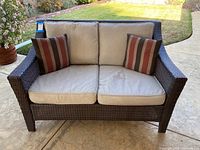 Front view of the loveseat showing beige cushions, dark synthetic wicker frame, and two striped accent pillows